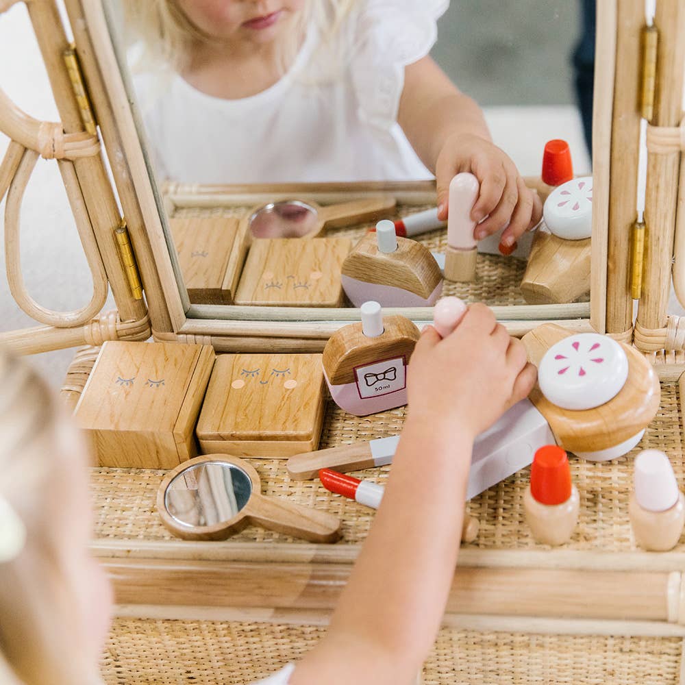 A child engages in imaginative play with the Wooden Beauty Kit on a wicker vanity, featuring a lipstick, compact, and non-toxic paint. Their reflection comes alive in the mirror as they explore each miniature cosmetic piece.