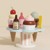 The Wooden Ice Cream Stand & Toppings features pastel-colored scoops, chocolate and raspberry sauce bottles, a cherry for topping, and a yellow spoon for delightful pretend serving. Perfect for role play fun.