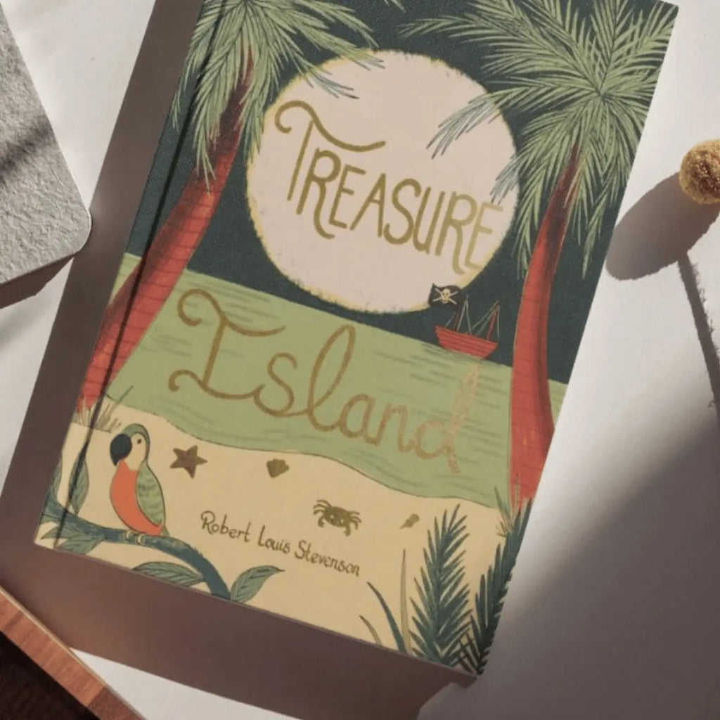 The "Treasure Island | Stevenson | Collector's Edition | Hardcover Book" rests on a white surface, featuring palm trees, a red ship, a parrot, a crab, and a golden sun on its tropical island-themed cover.