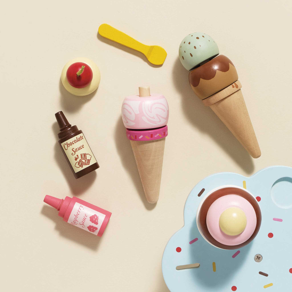 Experience role play fun with the Wooden Ice Cream Stand & Toppings, featuring cones, scoops, chocolate and strawberry sauces, a cherry on top, and a pastel blue plate with sprinkles. A spoon invites creativity—all beautifully arranged like a delightful gelato stand.