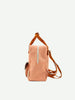 The Suzy Blush from Sticky Lemon's Envelope Collection is a peach-colored backpack made from recycled PET bottles, featuring brown straps, a front zipper pocket, and a shoulder handle. The plain light background accentuates its design.