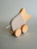 The Pull and Push Toy Little Wild Boar is a charming handcrafted toy featuring a wooden pig on wheels with a painted striped body, cheerful smile, and short string tail. Made from sustainable materials, it stands out beautifully against the plain gray background.