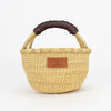 A woven basket with a dark brown leather handle.