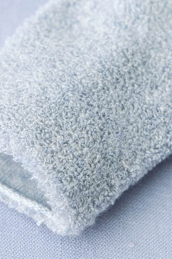 Close-up shot of a light blue terry cloth fabric, displaying its soft and textured surface. Reminiscent of Baby Pile Knit Socks - Blue made in Lithuania, the fabric appears folded or draped, with fine details of the looped fibers visible, giving it a plush and comfortable look.