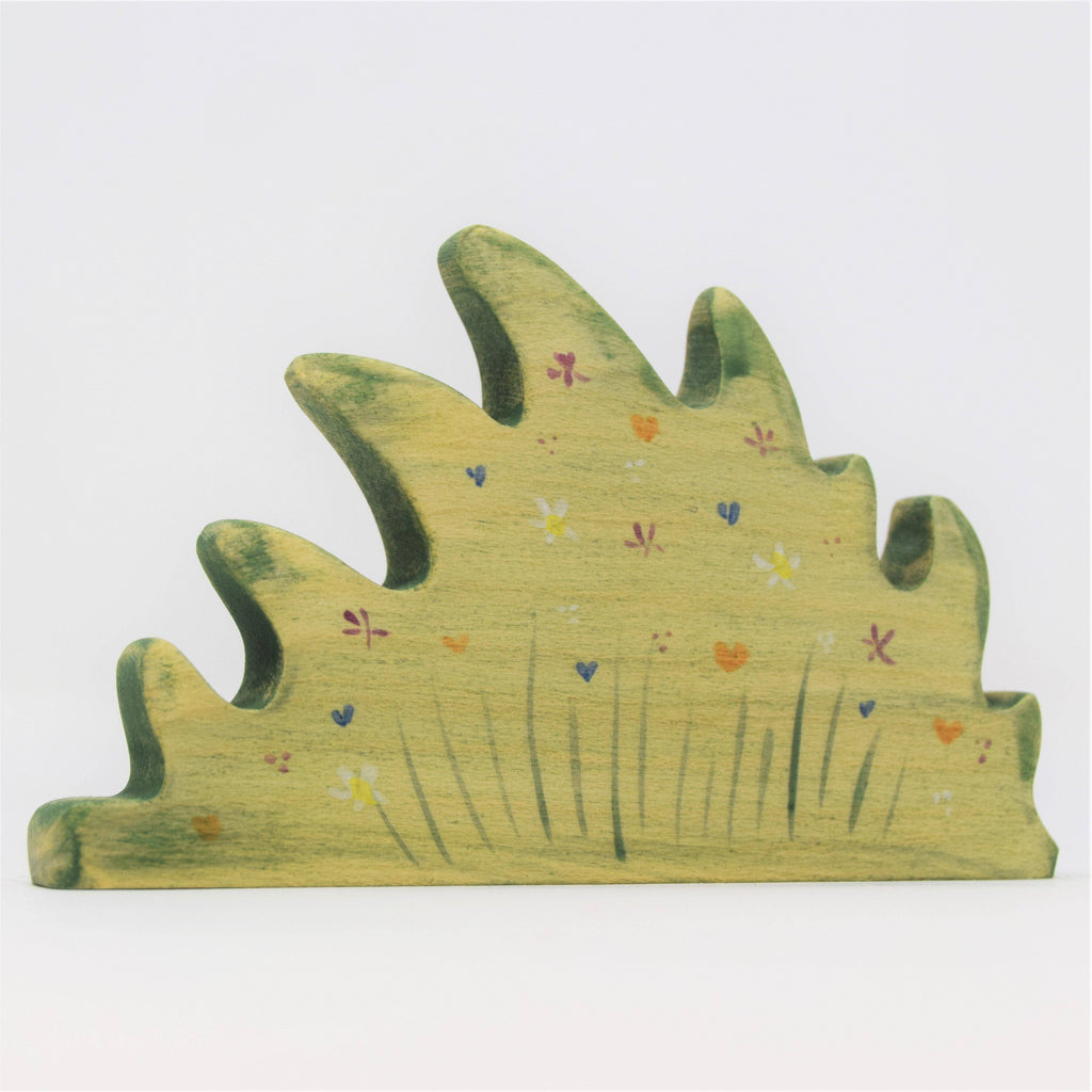 The Handmade Wooden Wildflower Patch is crafted from sustainable hardwood, shaped like a bush with green wavy edges, and adorned with colorful painted flowers and butterflies, using non-toxic plant-based stains for an eco-friendly touch.