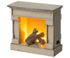 The Maileg Living Room Set includes a charming vintage-inspired fireplace model made of rustic wood, complete with faux logs and an internal glowing light for a cozy ambiance.
