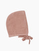 A soft, knitted baby bonnet in a muted pink color, perfect for Minikane Babies. The bonnet features a simple, textured knit design and has two ties at the bottom to secure it under the baby's chin. The background is plain white.

Minikane Doll Clothing | Élie Tea Pink Knit Bonnet