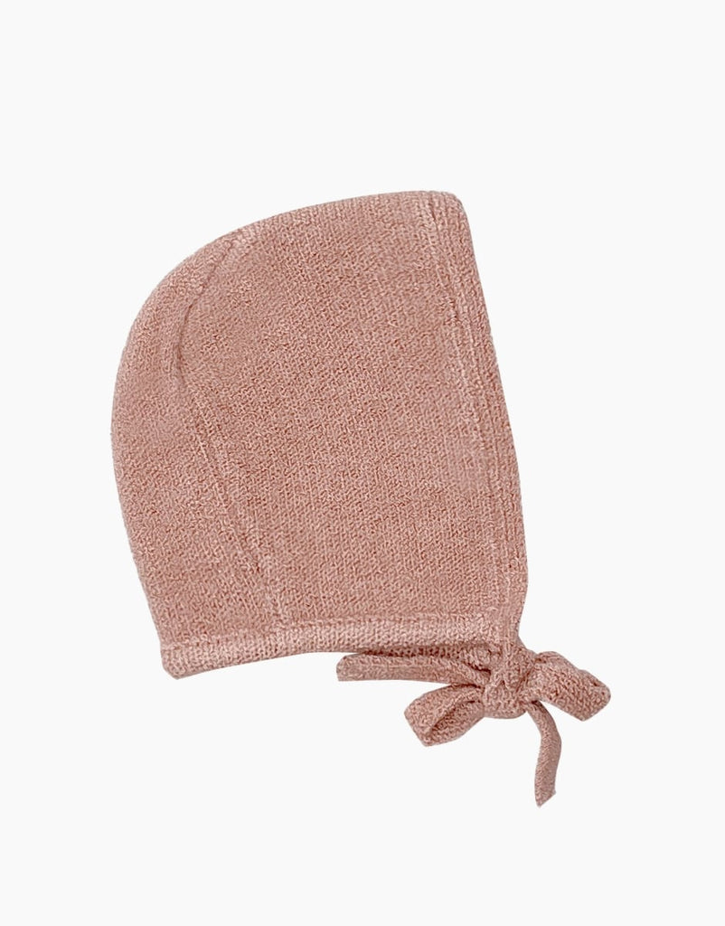 A soft, knitted baby bonnet in a muted pink color, perfect for Minikane Babies. The bonnet features a simple, textured knit design and has two ties at the bottom to secure it under the baby's chin. The background is plain white.

Minikane Doll Clothing | Élie Tea Pink Knit Bonnet