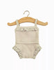 A Minikane Doll Clothing | Les P'tits Basique Girls' Underwear in ribbed linen knit and lace featuring a beige baby romper with spaghetti straps and ruffled trim on the chest and leg openings, hanging on a wooden hanger against a white background. The ribbed fabric adds texture and style reminiscent of popular Minikane Gordis dolls.