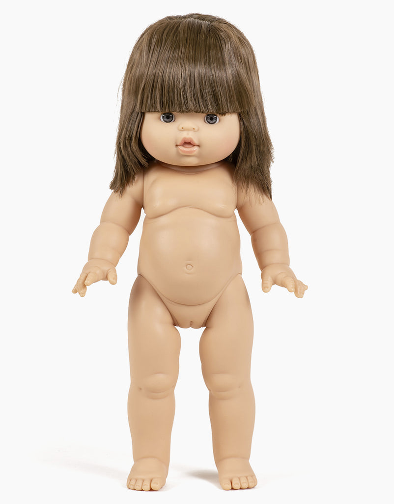 The Minikane Standing Doll (14") - Chléa With Clothing & Shoes features medium-length brown hair with bangs, articulated limbs, a neutral expression, and a gentle vanilla scent, enhancing its lifelike appeal. Displayed against a plain white background, it captures realistic charm.