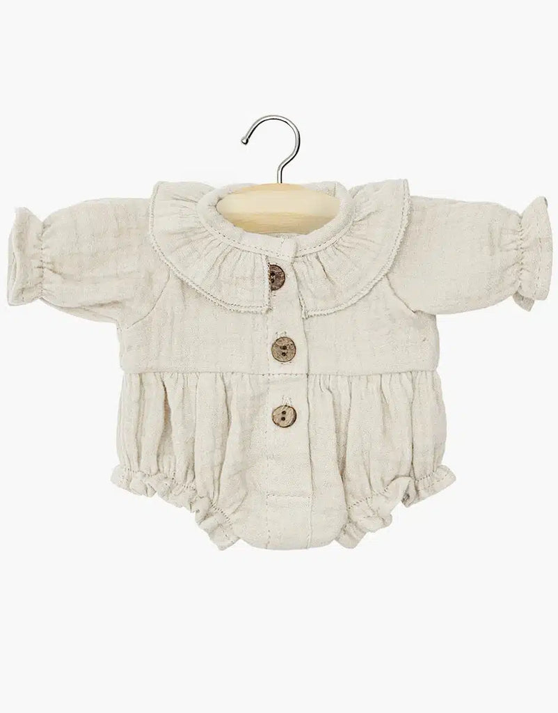 A beige, long-sleeved romper with a ruffled collar and cuffs, designed for the Minikane Sitting Doll (13"), hangs on a wooden hanger. It features three wooden buttons down the front and a gathered waist, complementing Charlie's anatomically correct form charmingly.
