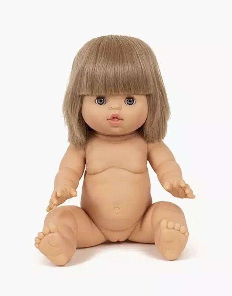 The Yzé Minikane Baby Doll With Sleeping Eyes (13") has lifelike features, including blue eyes and a natural vanilla scent. The doll, known for its anatomically correct details and short brown hair, is posed upright with slightly outstretched arms in a simple white background.