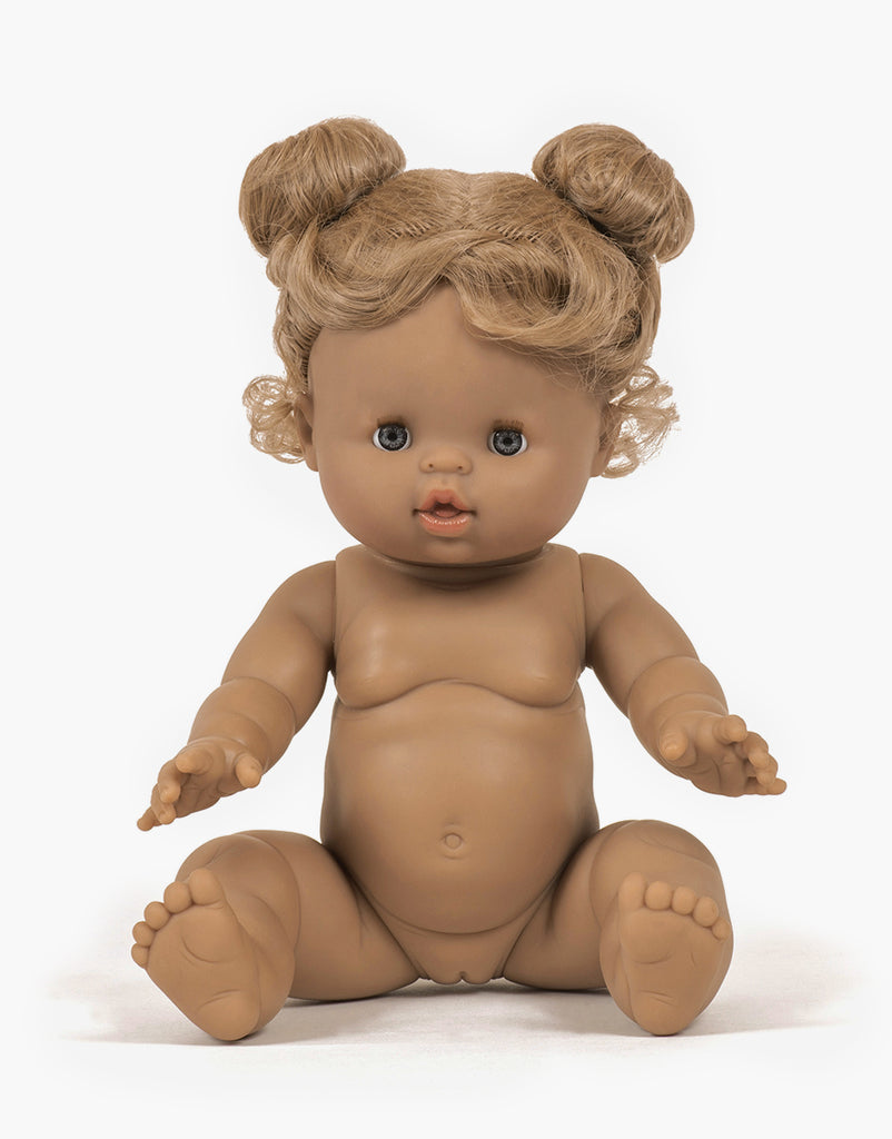 The Minikane Baby Doll (13") - Louise features brown skin, curly light brown hair in two buns, blue eyes, pink lips, outstretched hands and feet, and anatomically correct details. It has a natural vanilla scent and sits upright against a plain white background with outfit & sunglasses.