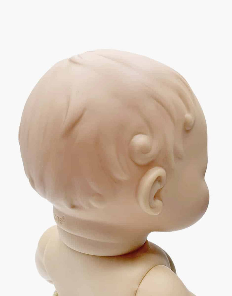 The image shows the back of a Minikane Doll (13") - Faustine with Green Romper, crafted from phthalate-free vinyl. It features detailed sculpted hair and soft curls on a fair complexion, with the head slightly turned right against a plain white background.