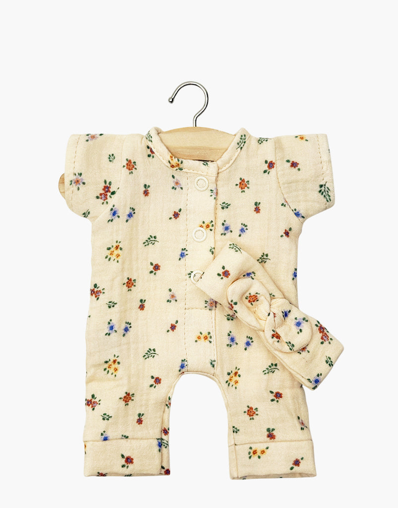 The Minikane Doll Clothing set includes the Lili Jumpsuit in Elise Cotton Gauze with a matching headband, adorned with small colorful flowers on beige fabric. This charming French-crafted baby romper hangs on a wooden hanger and is hand washable for easy care.