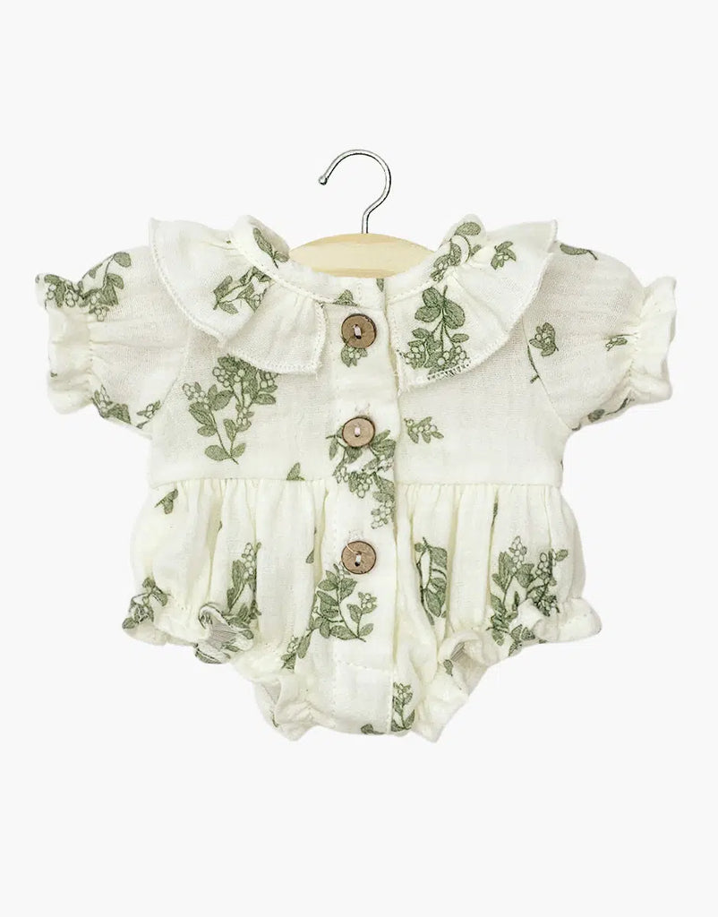 The Minikane Doll Clothing Leonore Romper, made in France, hangs on a wooden hanger. This short-sleeved piece features cream fabric with green foliage prints, a ruffled collar, and brown buttons down the front. It's charming and hand washable for easy care.