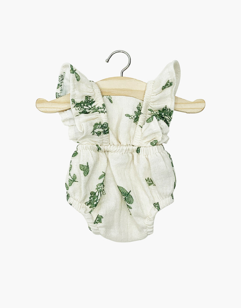 The Lou Retro Romper, crafted in France from cotton gauze and perfect for Minikane or 13" to 14" dolls, hangs on a wooden hanger. Its white fabric with a green floral pattern includes ruffled shoulder straps and an elastic waist, set against a plain white background.