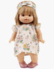 A Minikane doll with short blonde hair dons an Emile & Ida pink spring dress and matching headband in cotton, paired with purple sandals. Designed in France, this charming doll is hand washable for easy care.