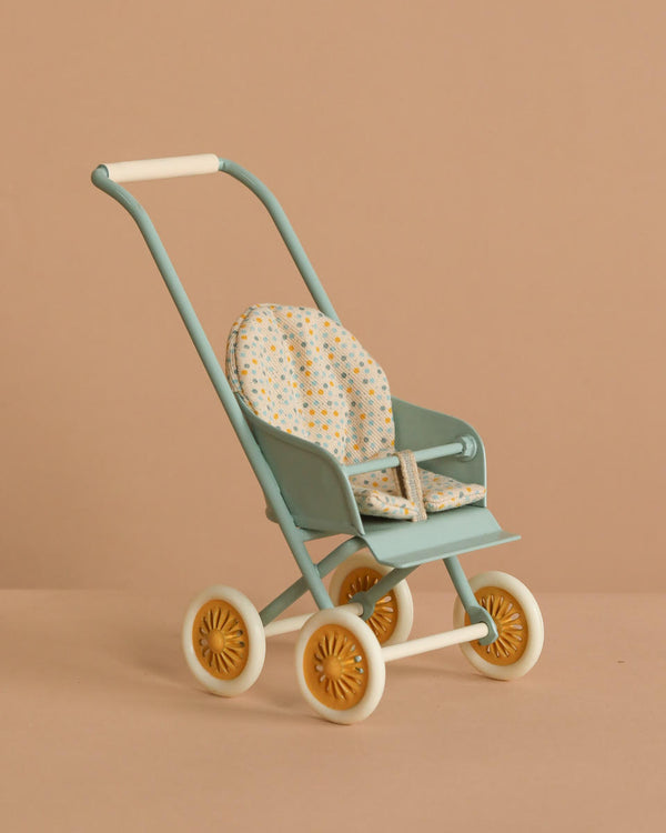 The Maileg Stroller, Micro - Mint is a small pastel green stroller with a patterned seat cushion and yellow wheels, set against a plain beige background.