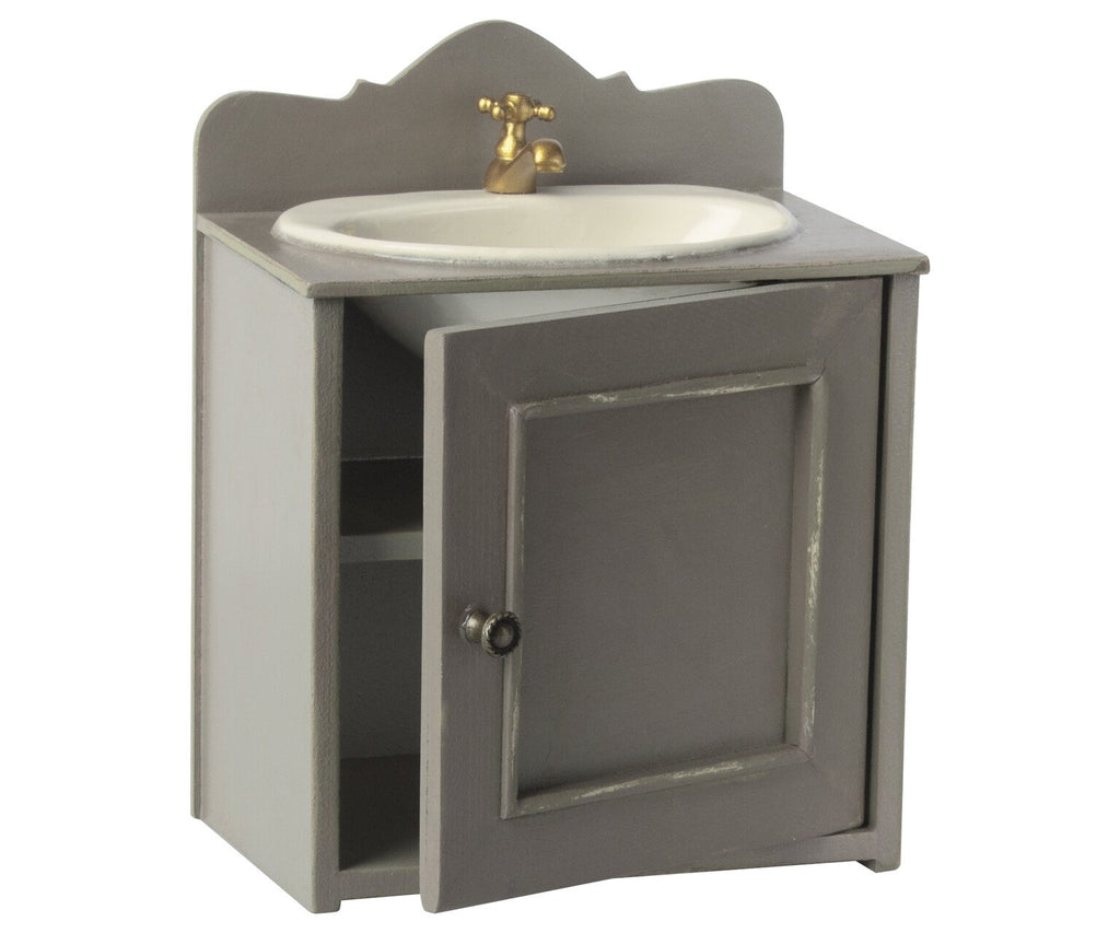 A Maileg miniature sink in gray with a vintage metal tap, featuring an open door revealing internal shelves.