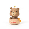 A Wooden Honey Bear Bobblehead figurine of a smiling bear sitting on a honey pot, with a small yellow bird perched on its head. The pot is labeled "honey" and has honey dripping.