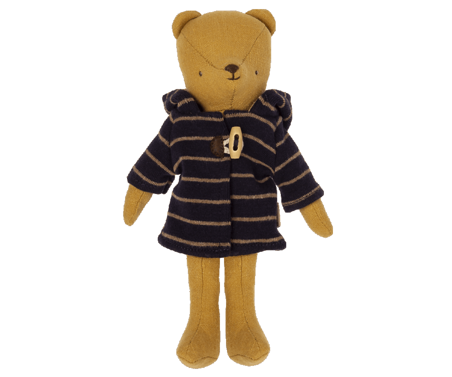 Teddy Junior, dressed in a light brown hue, wears the Maileg Extra Clothing: Duffle Coat featuring a dark blue hood with beige horizontal stripes and a toggle button. The plush teddy bear stands upright and has simple facial features with stitched eyes and nose.