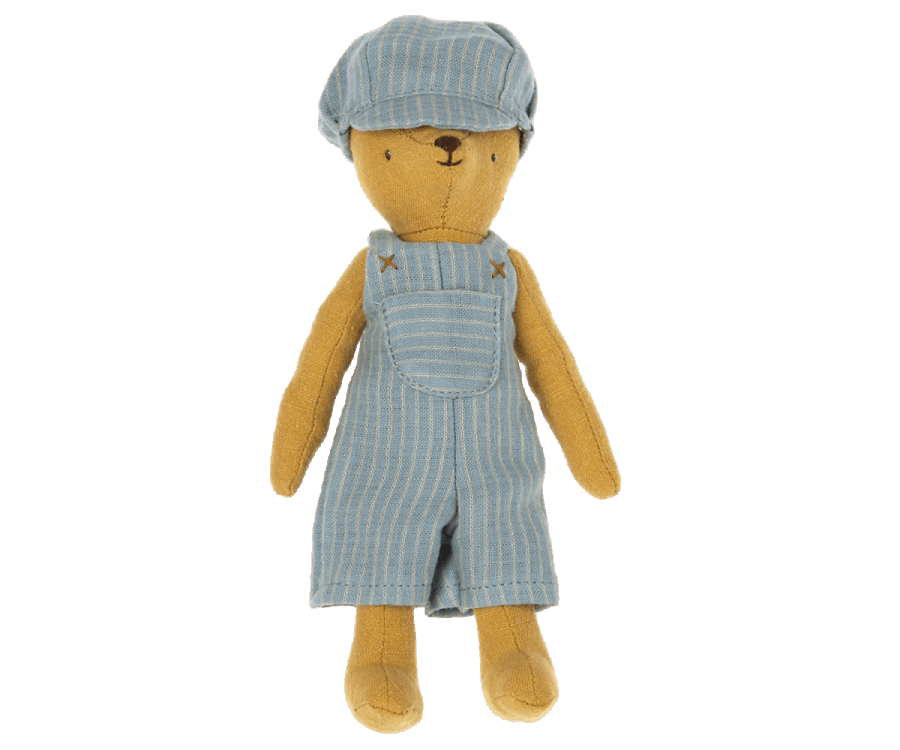 The bear named Teddy Junior is dressed in a blue and white striped outfit, consisting of overalls and a matching cap from the Maileg Extra Clothing collection. This outfit, which can be purchased separately as "Overall and Cap for Teddy Junior," dresses the brown teddy bear that stands upright with its arms at its sides.