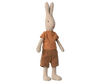 A Maileg Rabbit Size 1 - Classic T-shirt & Shorts standing upright, dressed in a striped orange and yellow shirt and brown shorts. The bunny, made from natural linen, has long ears, a small black nose, and stitched facial features, giving it a cute and friendly appearance.