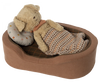 A toy dog bed with a toy dog laying in the bed with a pillow and a blanket.