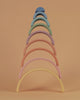 A colorful Raduga Grez 9-piece rainbow stacker consisting of arches in various pastel colors arranged in size order against a pale orange background.