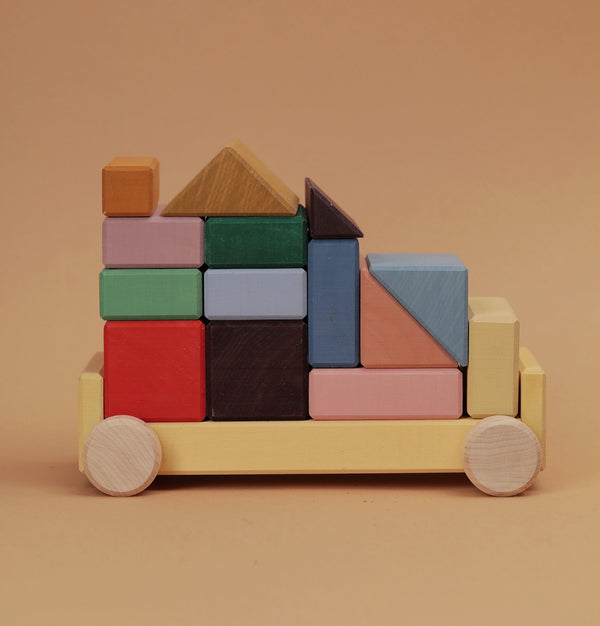 The Raduga Grez Vehicle Blocks is a solid wood toy vehicle with colorful, eco-friendly painted blocks featuring rectangles, squares, and triangles. It has wheel-like circles on the base, creating a simple racing car design.