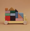 The Raduga Grez Vehicle Blocks is a solid wood toy vehicle with colorful, eco-friendly painted blocks featuring rectangles, squares, and triangles. It has wheel-like circles on the base, creating a simple racing car design.