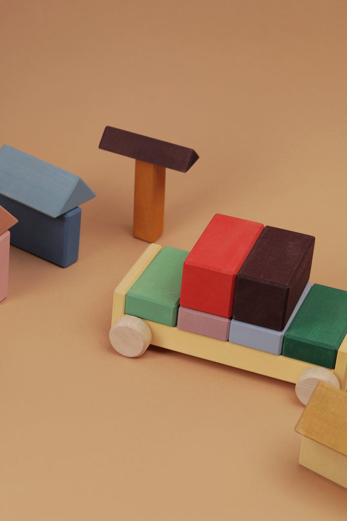 Raduga Grez Vehicle Blocks, crafted from solid wood and painted with eco-friendly colors, form a racing car using red, black, and green blocks on a beige surface, while the houses feature pink, blue, and yellow hues.