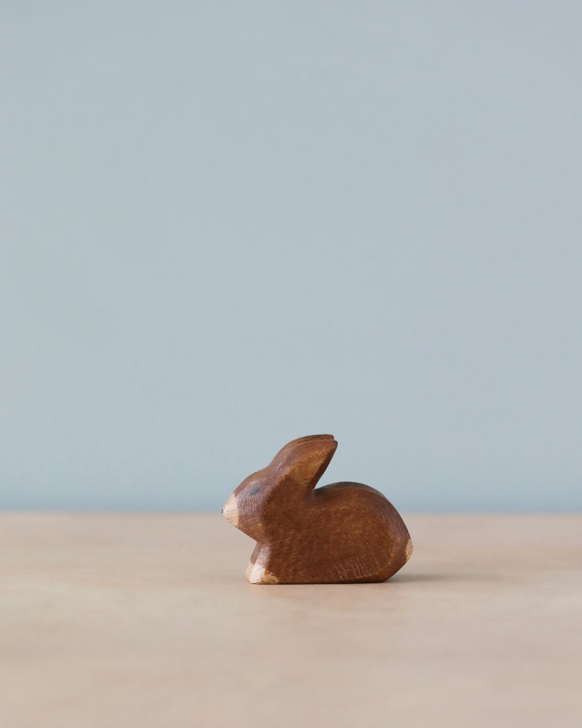 A small, sustainable Handmade Holzwald Small Brown Rabbit figurine on a plain surface with a pale blue background. The figurine is minimalist with smooth, stylized curves.