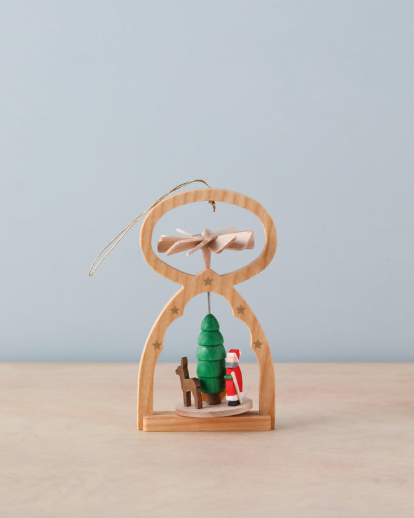 The Richard Glaesser Mini Pyramid Hanging Ornament - Santa features a German-made small wooden arch with stars, showcasing a Santa, green tree, and reindeer. It has a delicate propeller and handy hanging string against a soft blue background.