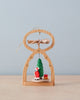The Richard Glaesser Mini Pyramid Hanging Ornament - Santa, made in Germany, features a green tree with Santa on a sled, a propeller, and star details. It rests on light wood against a pale blue background.