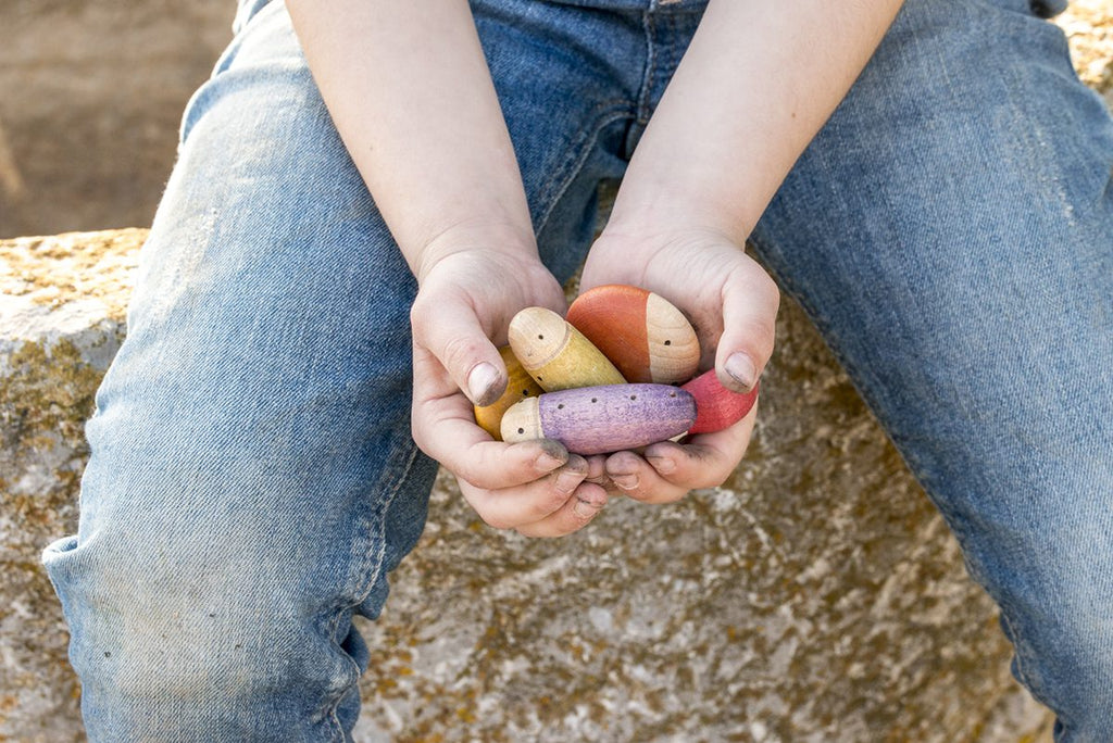 A child holding Grapat Insects, dyed with non-toxic dyes, in their cupped hands, seated outdoors with denim jeans visible, emphasizing themes of playfulness and simplicity.