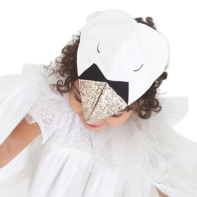 A young child with curly hair wearing a Meri Meri Swan Costume with sparkling gold beak details, looking downward with tulle wings spread.