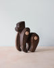 The Handmade Wooden Gorilla features a smooth, minimalist design with prominent wood grain and lighter circular joints, standing on a light surface against a plain pale blue background.