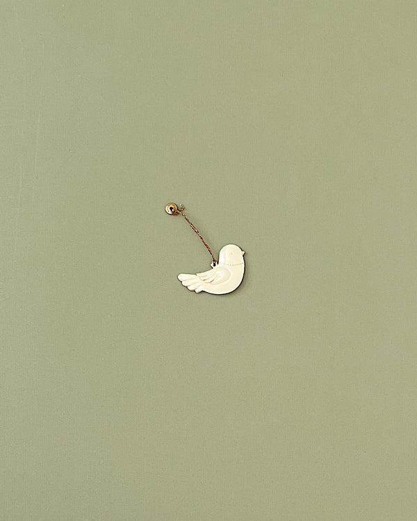 A Maileg Metal Bird Ornament, reminiscent of Maileg ornaments, is suspended by a thin string from a small mounted pin against a plain, light green background. The white bird, with minimal details, appears to be in mid-flight—an elegant touch for any home decoration or Christmas tree.
