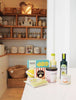 Various grocery set items like crackers, popcorn, and oils displayed on a kitchen countertop with open wooden shelves filled with baskets, toddler kitchen accessories, and kitchen essentials in the background.