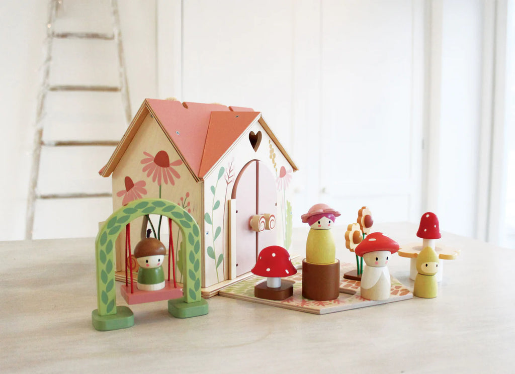 The Rosewood Cottage playset brings a woodland cottage to life with floral-adorned house, swing featuring a mushroom-headed figure, and multiple mushroom-shaped figures. It rests on a light table, complemented by a ladder to complete the enchanting meadow scene.