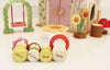 The Rosewood Cottage set charmingly displays four wooden peg dolls with flower-themed designs—Flora, Corny, Bud, and Joey—in front of a woodland cottage. The enchanting scene includes a toy house with a swing and delicate floral accents, evoking the magic of an imaginative meadow.