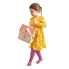 A young girl in a yellow polka dot dress and pink tights carries the Rosewood Cottage toy birdhouse with a pink roof and decorative plants. She walks barefoot against a white background, echoing the charm of a magical woodland cottage.