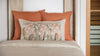A cozy bedroom scene featuring a neatly made bed with a beige cover and two orange pillows with one Coral & Tusk Mushroom Forest Pocket Pillow in front.