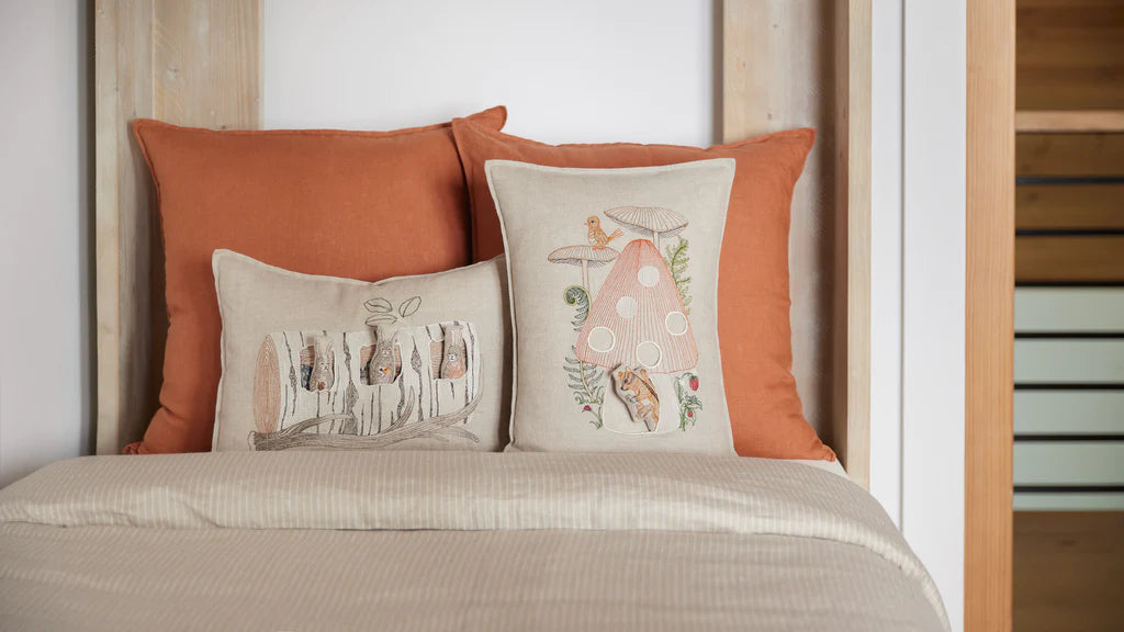 Two Coral & Tusk Aspen Log Bunnies Pocket Pillows are propped on a bed with Oeko-Tex Certified terracotta-colored pillowcases in a cozy, well-lit bedroom setting.