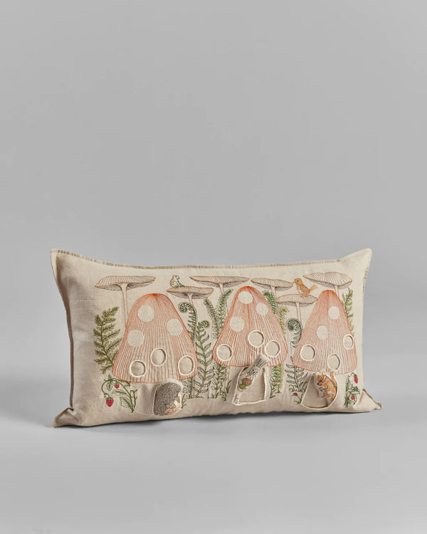 Rectangular decorative Coral & Tusk Mushroom Forest Pocket Pillow with embroidered mushroom house designs in natural tones on a beige background, displayed against a light grey backdrop.