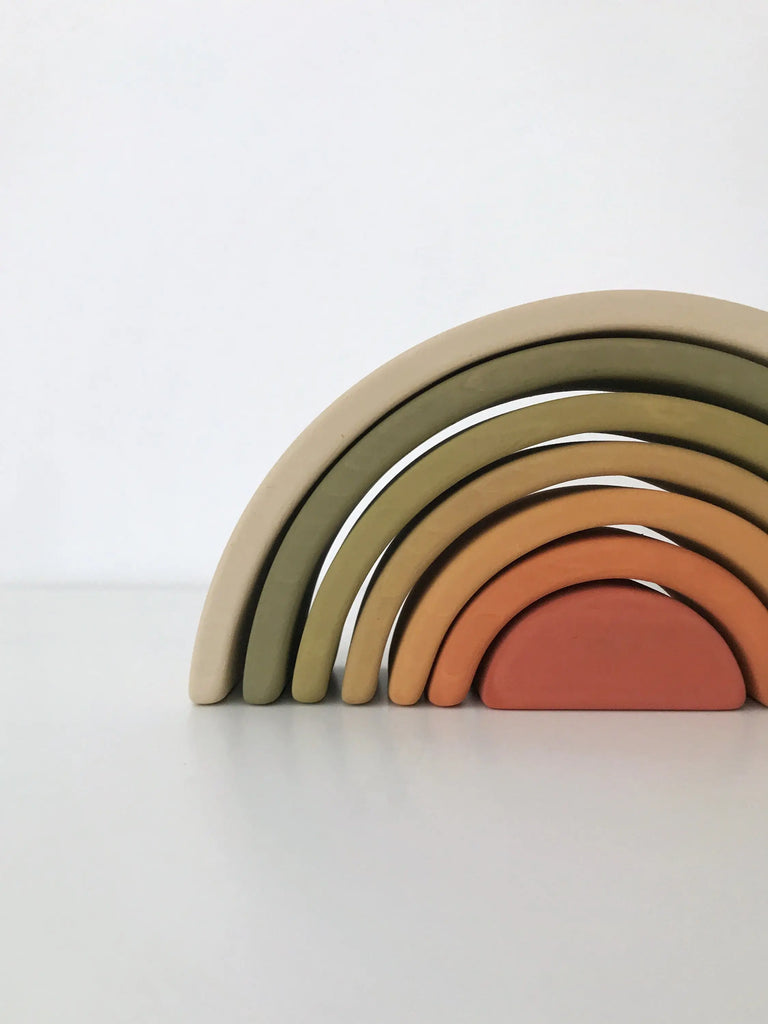 A stack of wooden Handmade Mini Rainbow Stacker - Flower Meadow toy pieces in muted colors, painted with non-toxic paint, arranged against a white background with the largest arch on the bottom and the smallest on top.