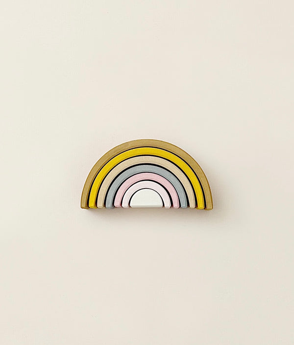 A stacking toy with 7 pastel tone wooden arcs stacked into a rainbow shape. 