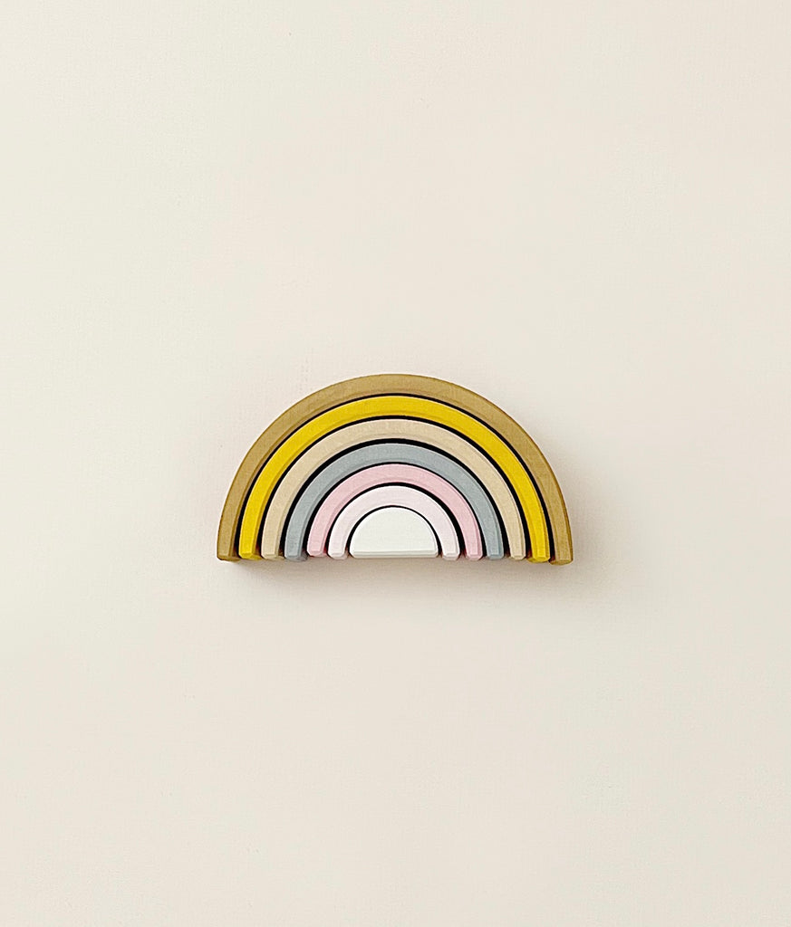 A stacking toy with 7 pastel tone wooden arcs stacked into a rainbow shape. 